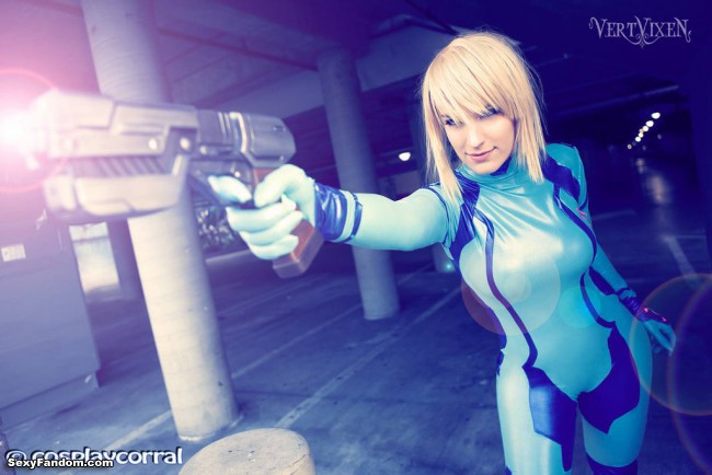 Young woman in Zero Suit Samus costume poses holding prop pistol in firing position.